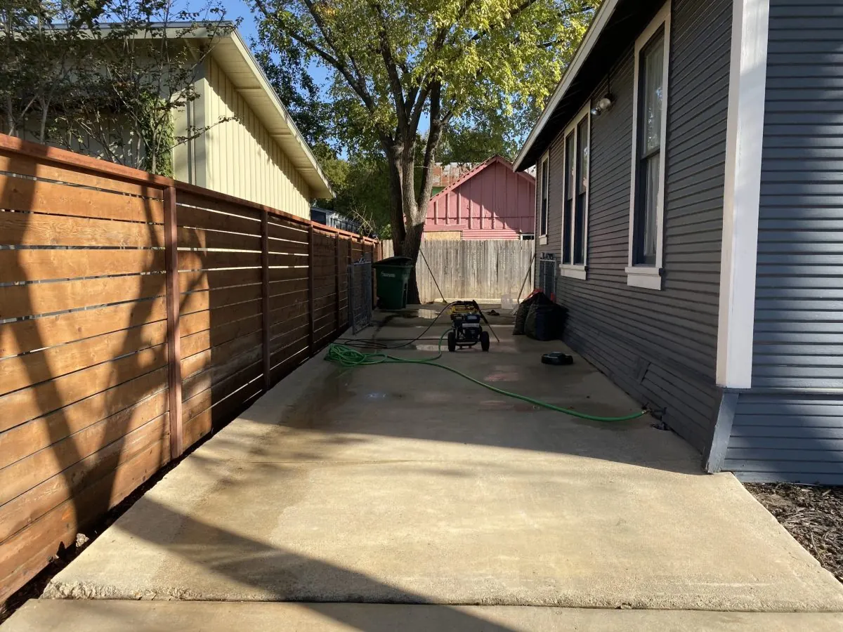 Clean concrete side yard beside a wood fence and gray siding